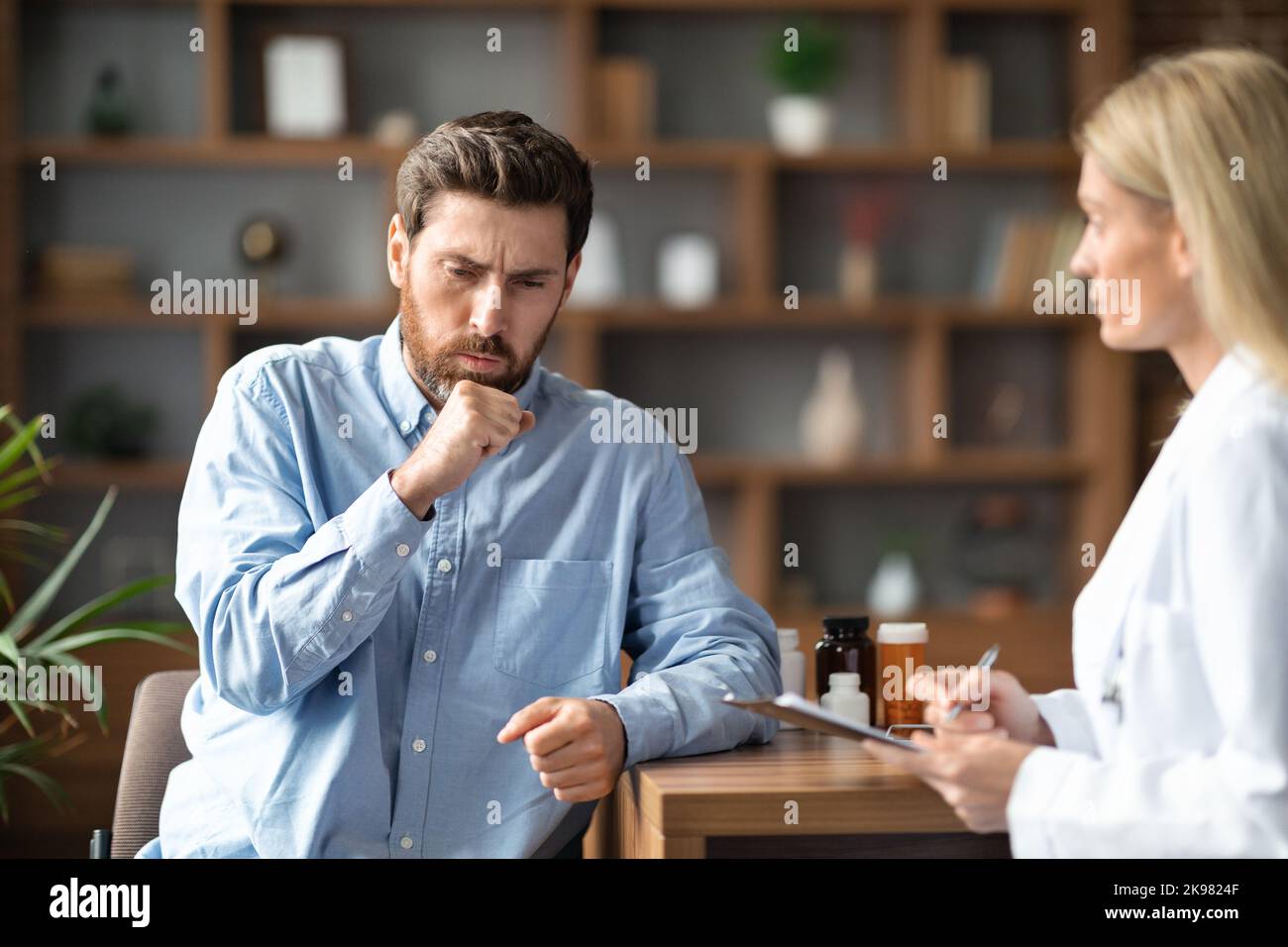 Kranker Junger Mann Hustet Während Eines Treffens Mit Einer Ärztin In Der Klinik Stockfoto