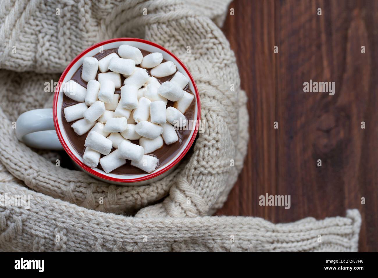 Von oben ein Becher heißer Schokolade mit Marschwalben, umgeben von einem beigefarbenen Wollschal auf einem Holztisch Stockfoto
