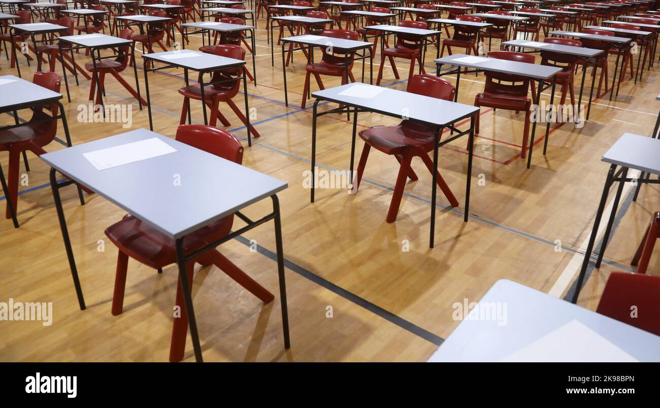 Reihen mit ordentlich angeordneten Untersuchungstischen oder Schreibtischen mit roten Stühlen. Große Schulhalle oder großer Raum, bereit für Schülerprüfungen oder Testprüfungen. Stockfoto