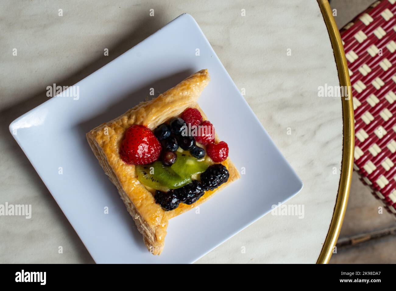 Ein viereckiges, mit Früchten gefülltes französisches Blätterteig auf einem weißen viereckigen Teller. Auf dem mit Sahnehühnchen gefüllten Dessert befinden sich Erdbeeren, Kiwi und Brombeeren Stockfoto