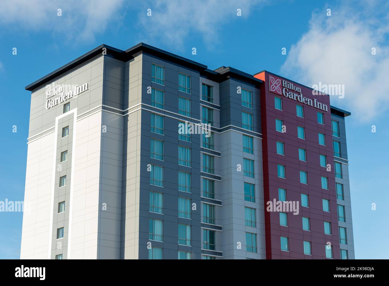 Hilton Garden Inn Hotel, ein neu erbautes, hohes Gebäude mit Metall-Verbundpaneelen in Grau, Rot und Hellgrau vor einem hellblauen Himmel und Klo Stockfoto