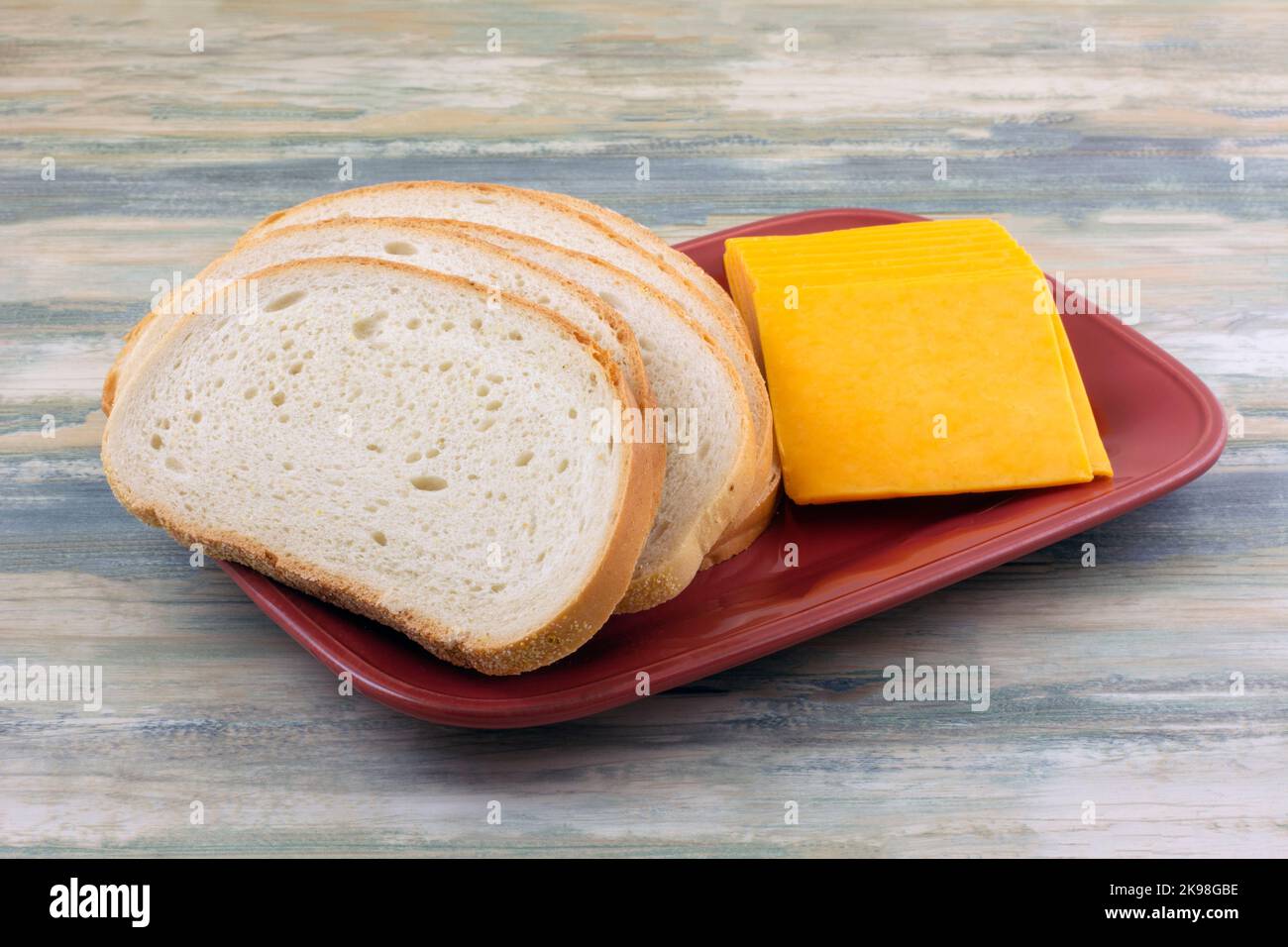 Sauerteig-Brot und Käsescheiben auf rotem Servierteller zur Vorbereitung für gegrillte Käse-Sandwiches Stockfoto