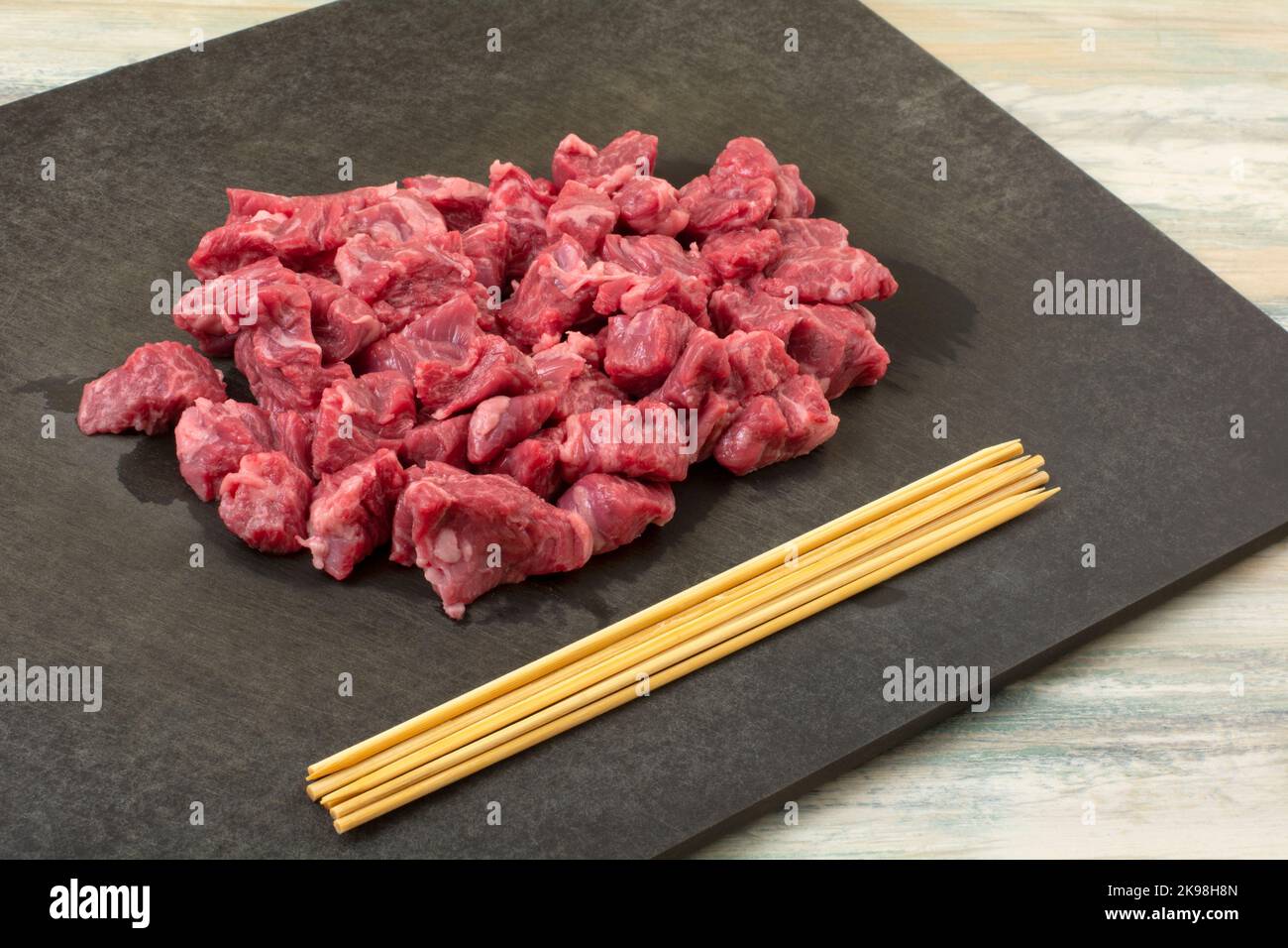 Roh Beef Bavette Sirloin Steak Würfel und Holzspieße auf schwarzem Schneidebrett Stockfoto