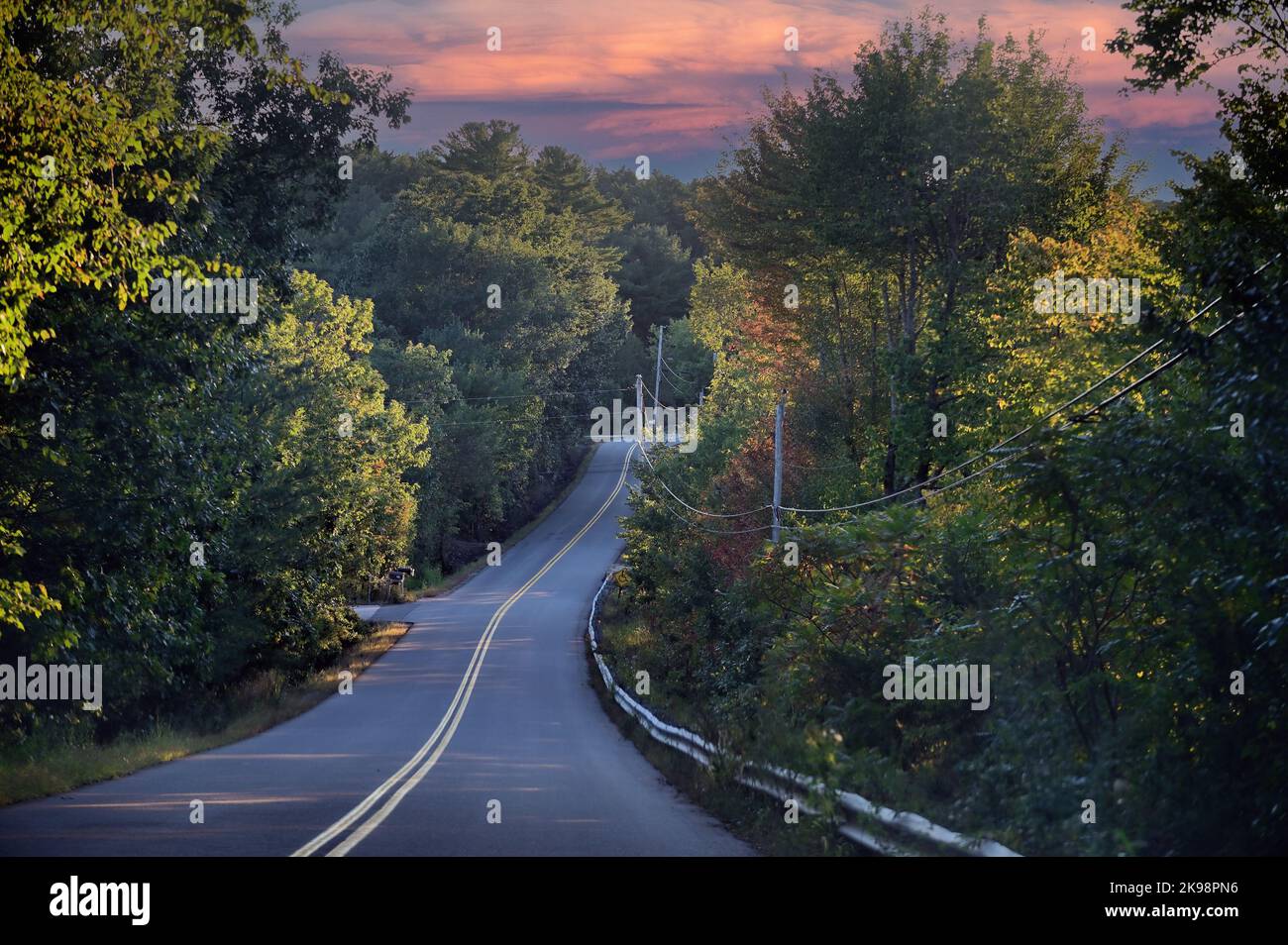 Wells, Maine, USA. Frühe Anzeichen des Herbstes beginnen, in den Bäumen entlang eines schmalen, leeren Streifens der Autobahn im südlichen Maine zu erscheinen. Stockfoto