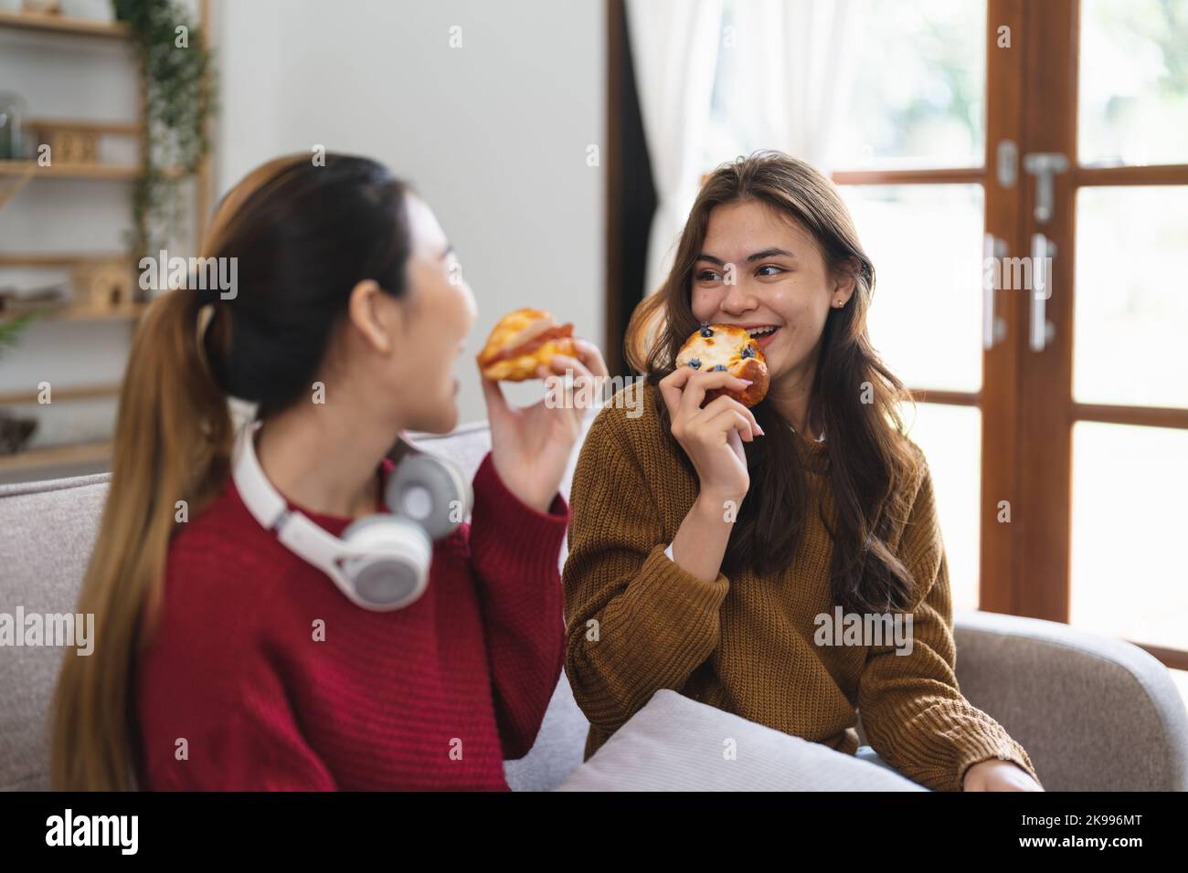 Zwei Freunde genießen es, Croissants zu essen, die auf einer Couch im Wohnzimmer zu Hause sitzen Stockfoto
