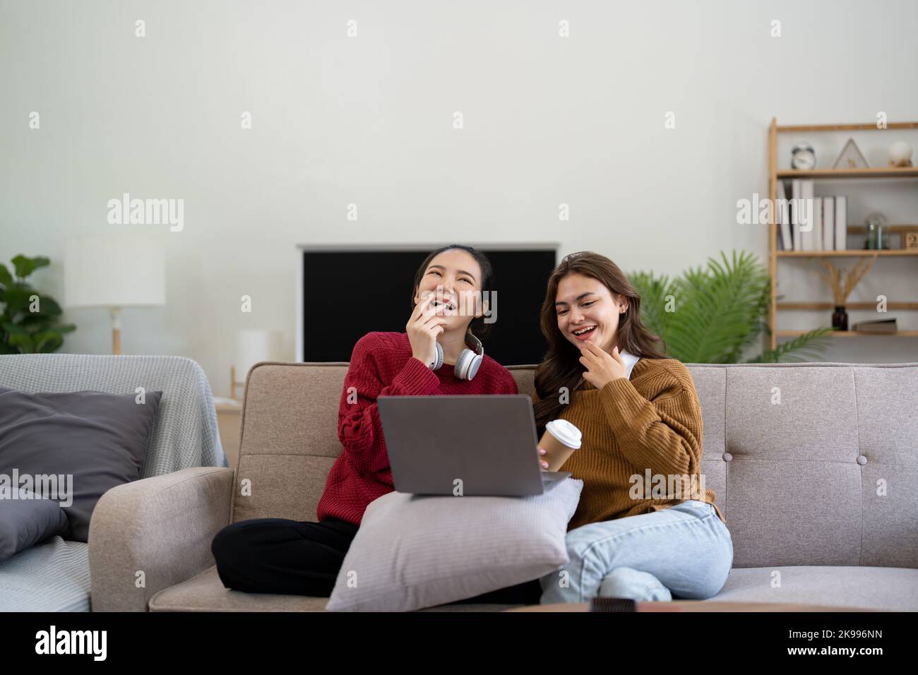 Asiatische Freundinnen sitzen im Wohnzimmer und schauen sich gemeinsam einen Film auf dem Laptop an. Moderne Freundschaften mit Frauen Genießen Sie den Lifestyle mit Aktivitäten am Wochenende über WLAN Stockfoto