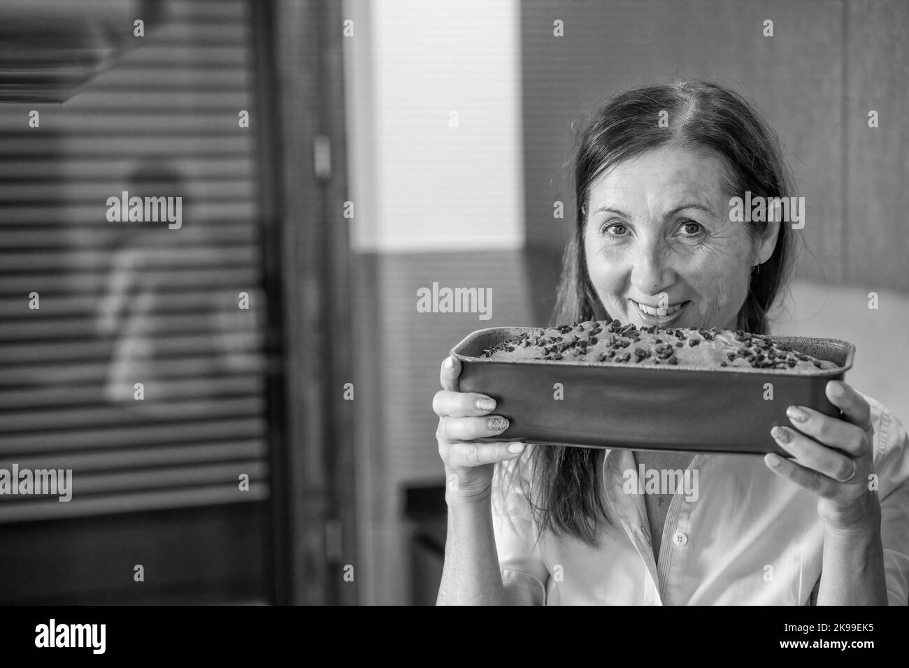 Glückliche Frau hält ein Brett mit einem leckeren Kuchen und schnuppert den hausgemachten Kuchen. Stockfoto