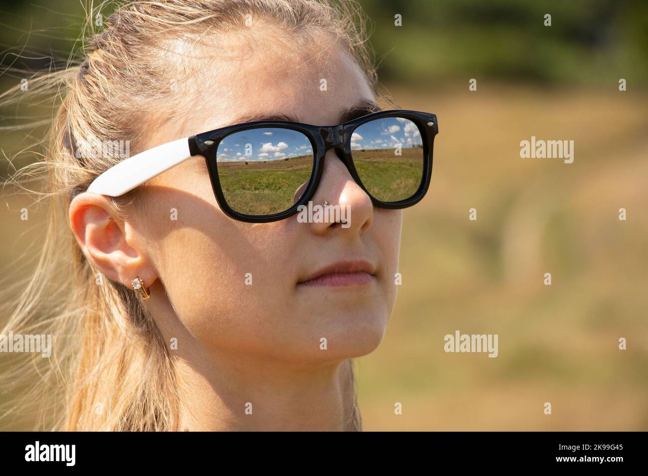 Gesicht eines Mädchens in Sonnenbrillen Nahaufnahme, Reflexionen in Gläsern des Feldes und des Himmels im Sommer Stockfoto