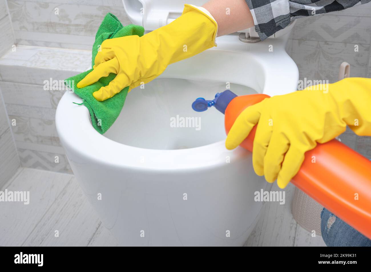 Nahaufnahme Hand mit Waschmittel Reinigung Toilettenschüssel im Badezimmer. Mann in gelben Gummihandschuhen, der Toilettensitz mit grünem Tuch reinigt. Badezimmer und Toilette Stockfoto