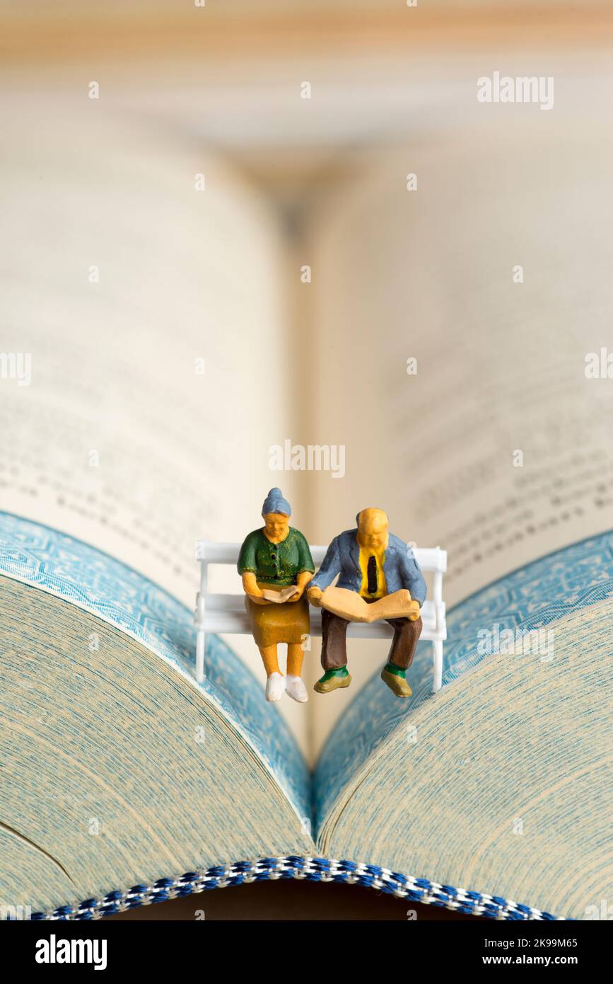 Nahaufnahme von Miniaturfiguren eines älteren Paares, das Buch und Zeitung auf einer Bank las. Stockfoto
