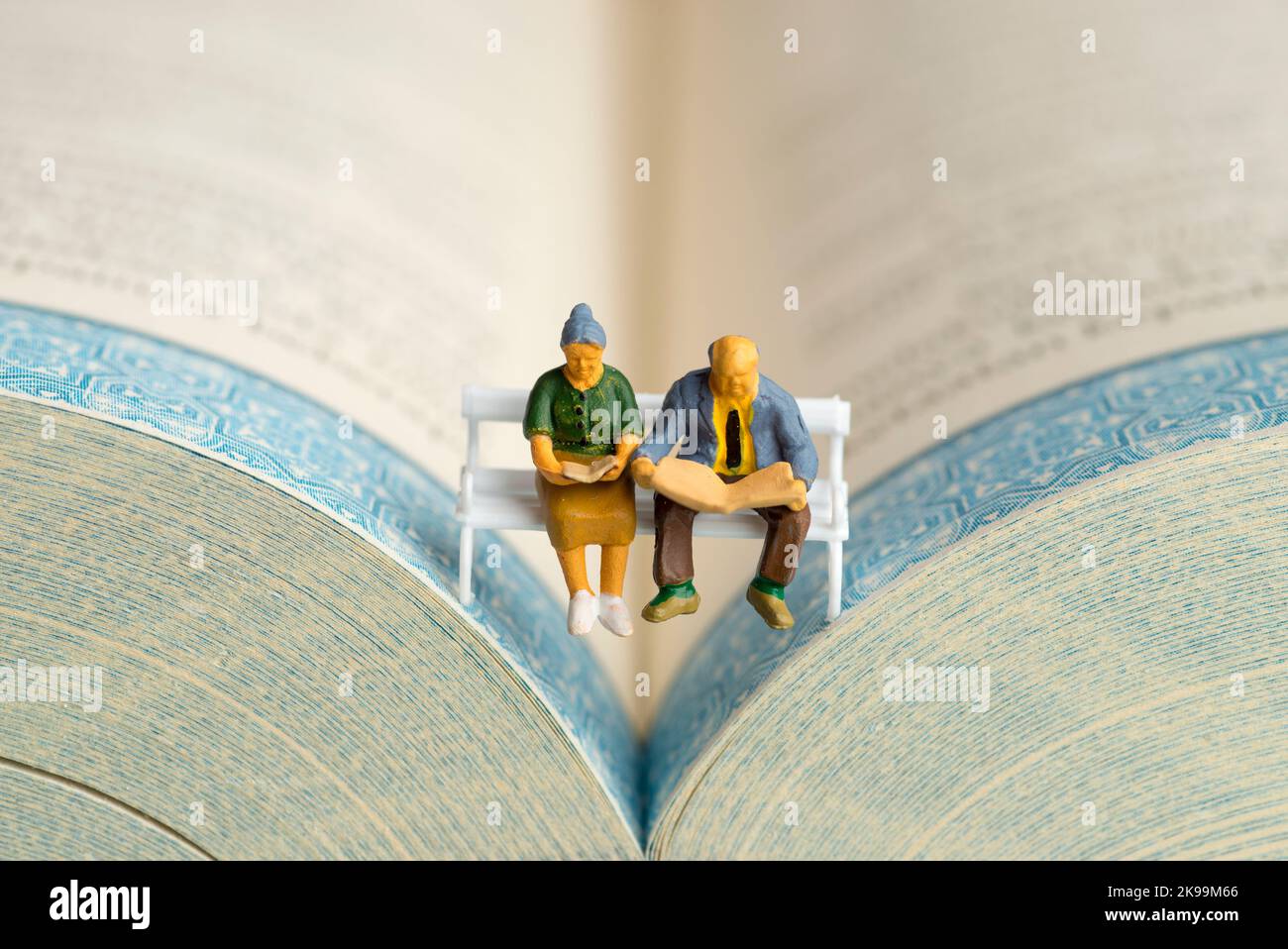Nahaufnahme von Miniaturfiguren eines älteren Paares, das Buch und Zeitung auf einer Bank las. Stockfoto