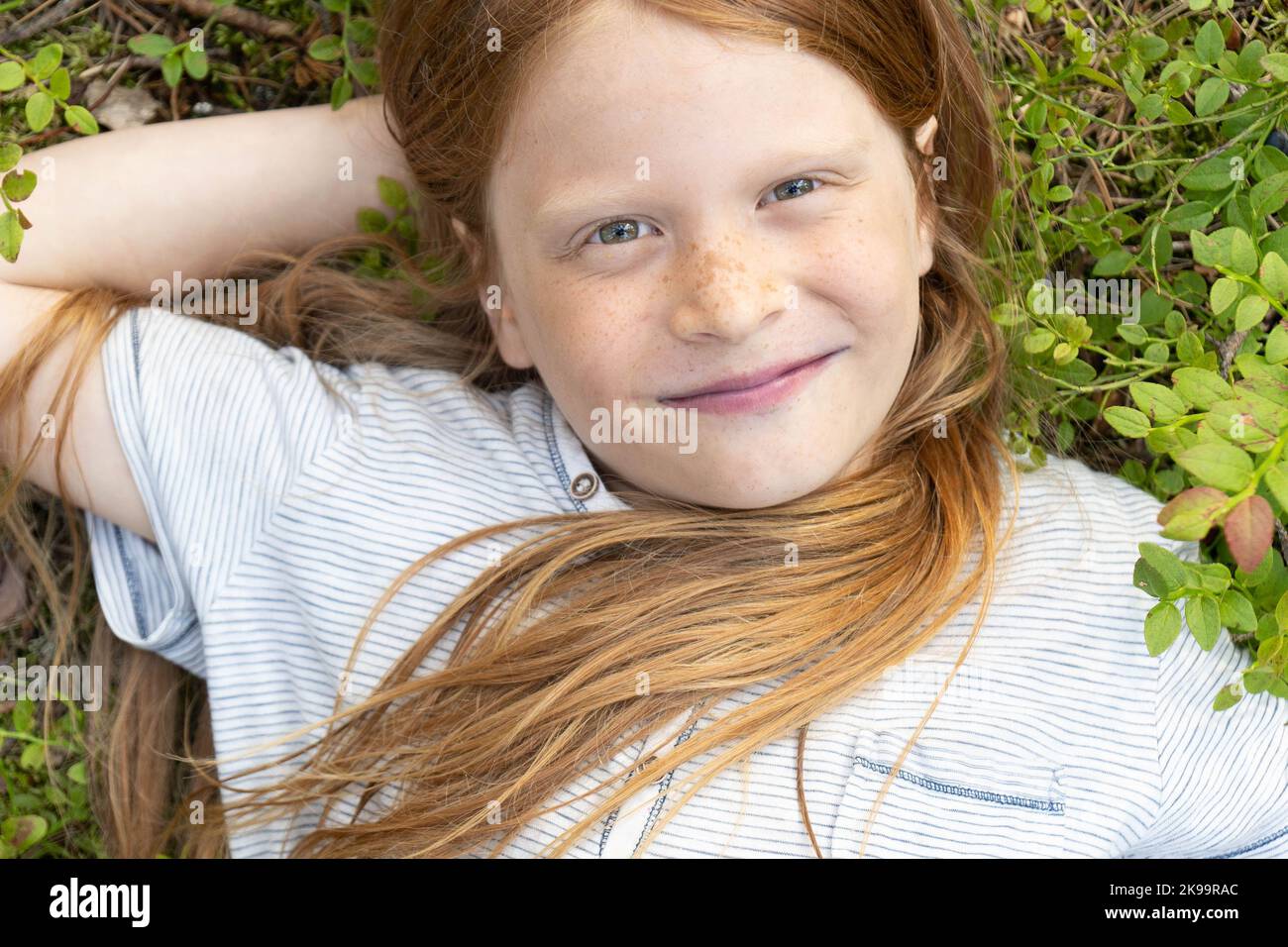 Porträt eines rothaarigen Jungen mit langen Haaren auf dem Gras. Flach liegend.der glückliche Junge lächelt. Speicherplatz kopieren. Stockfoto