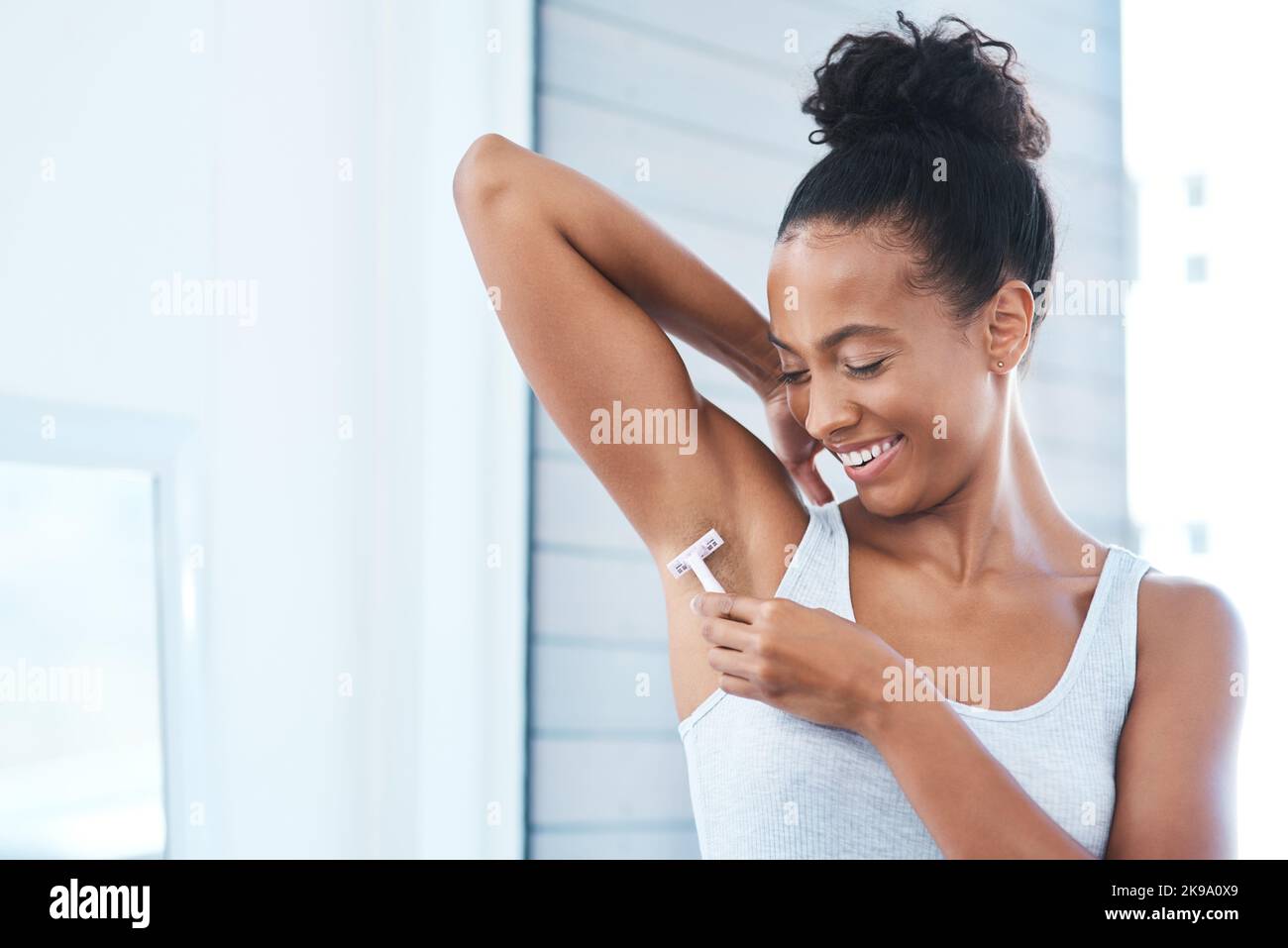Sie durchläuft ihr tägliches Ritual. Eine attraktive junge Frau, die ihre Achselhöhlen mit einem Rasiermesser im Badezimmer rasieren kann. Stockfoto