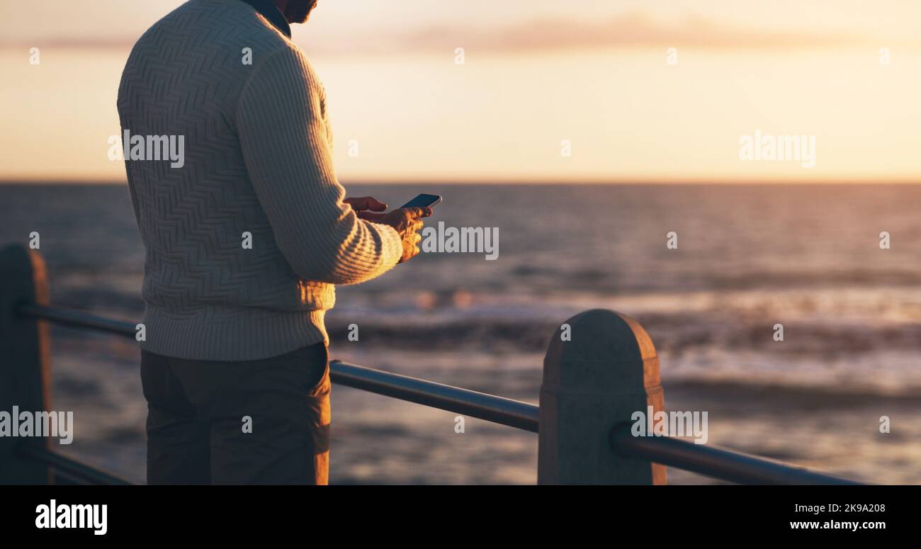 Ich werde heute Abend etwas spät nach Hause kommen. Rückansicht eines Mannes, der sein Handy am Strand benutzte. Stockfoto