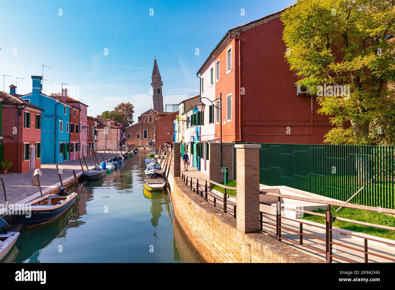 Kanal mit Booten und bunten Häusern der Insel Burano in Venedig, Italien. Die Kirche des heiligen Martin Bischof im Hintergrund. Stockfoto