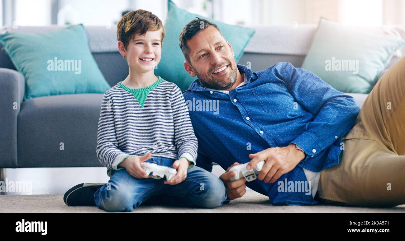 HES wird zu einem ernsthaften Gamer von Tag zu Tag. Ein fröhlicher Vater und Sohn spielen Videospiele zusammen, während sie auf dem Boden zu Hause sitzen. Stockfoto