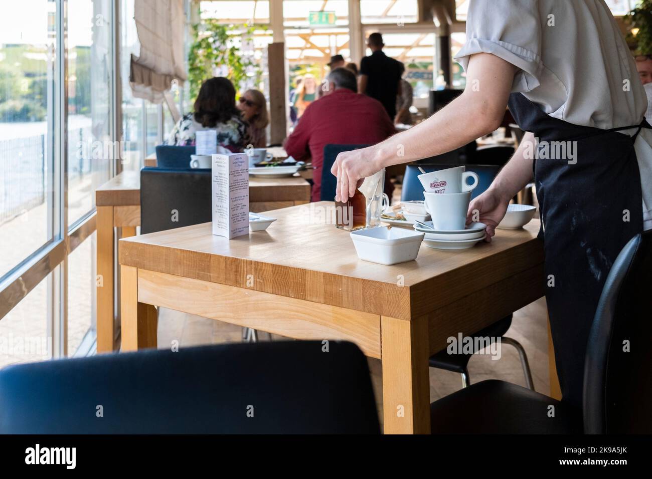 Ein Küchenmitarbeiter, der Tische in einem belebten Restaurant in Newquay in Cornwall im Vereinigten Königreich abräumte. Stockfoto