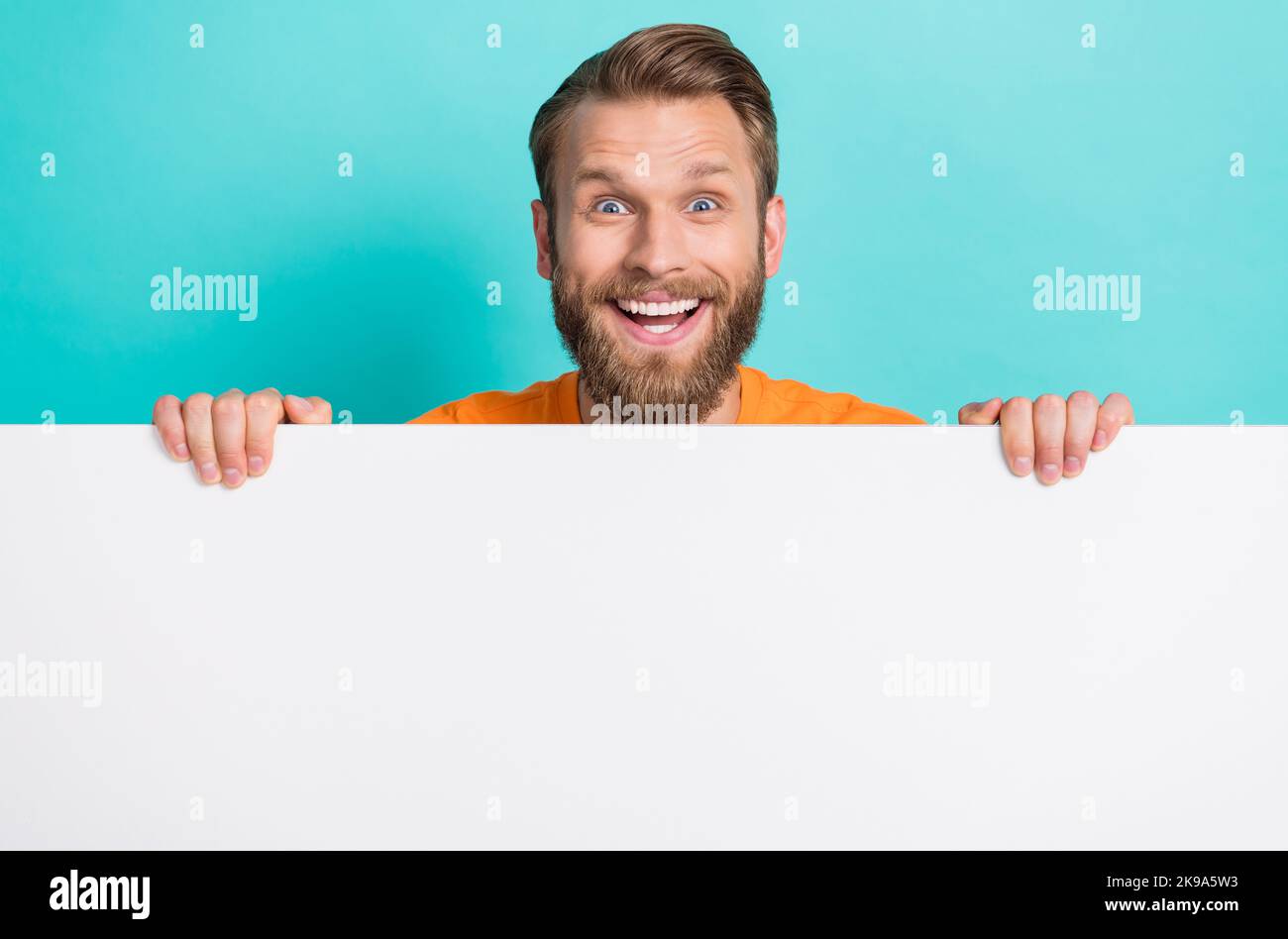 Foto von beeindruckt braun Frisur Kerl halten promo tragen orange T-Shirt isoliert auf teal Farbe backgroiund Stockfoto