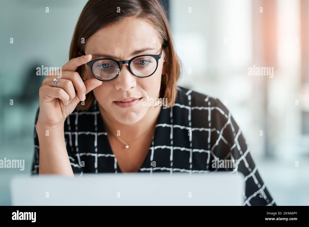 Das muss genauer hingeschaut werden. Eine junge Frau, die in einem Büro an einem Laptop arbeitet. Stockfoto