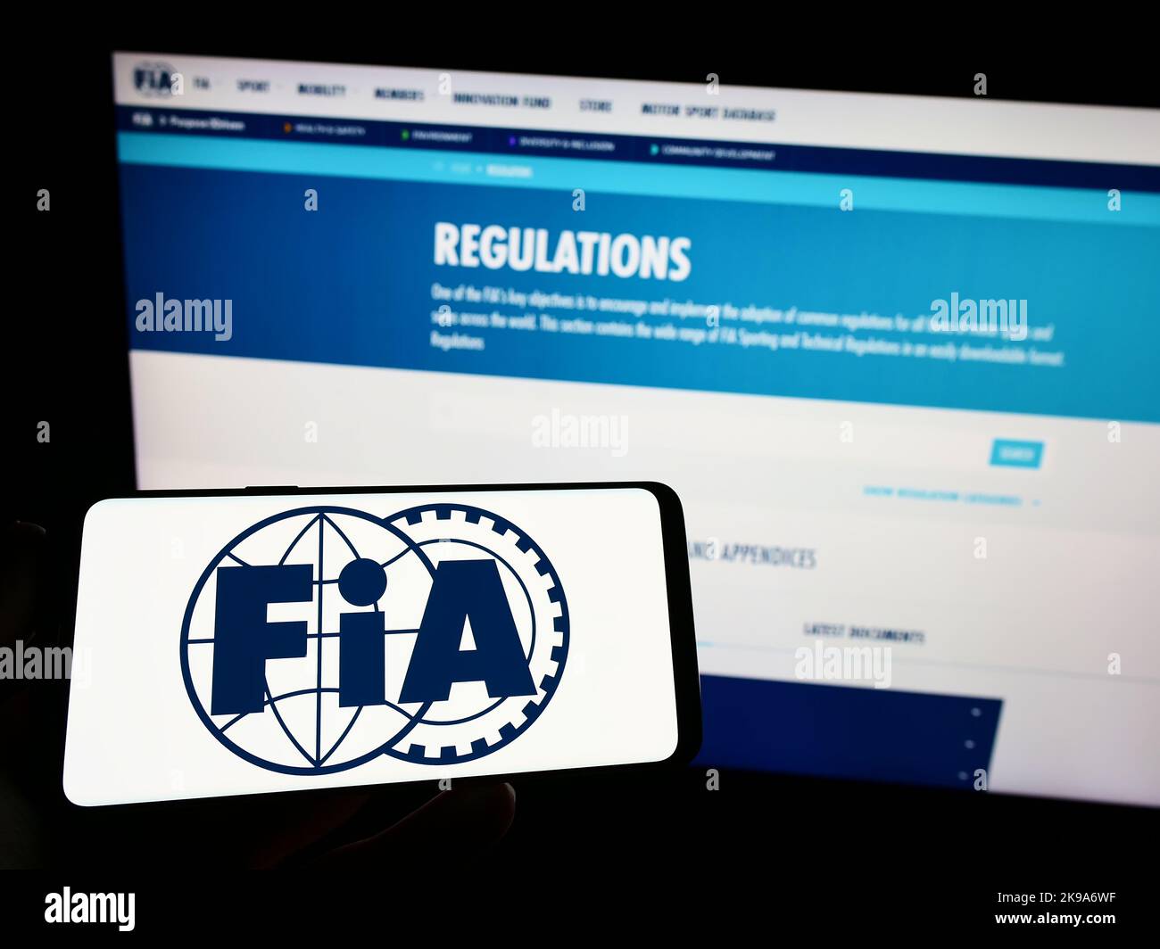Person, die das Mobiltelefon mit dem Logo der Internationalen Automobilföderation (FIA) auf dem Bildschirm vor der Webseite hält. Konzentrieren Sie sich auf die Telefonanzeige. Stockfoto
