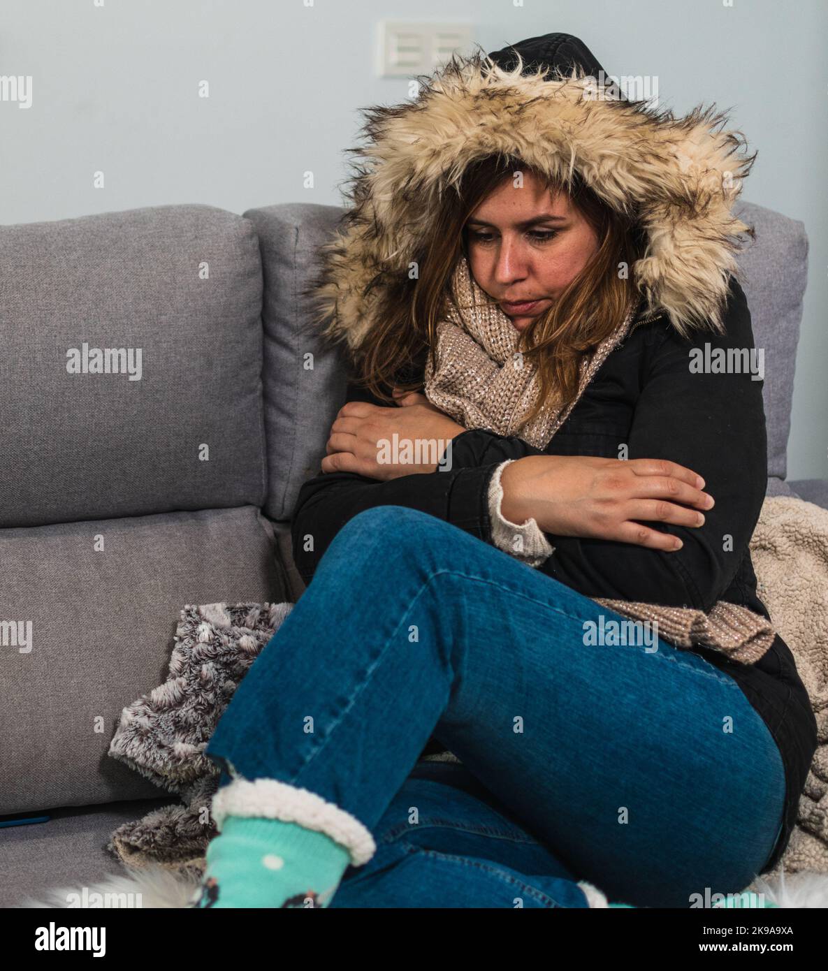 Frau friert zu Hause in einem Wintermantel auf dem Sofa Stockfoto