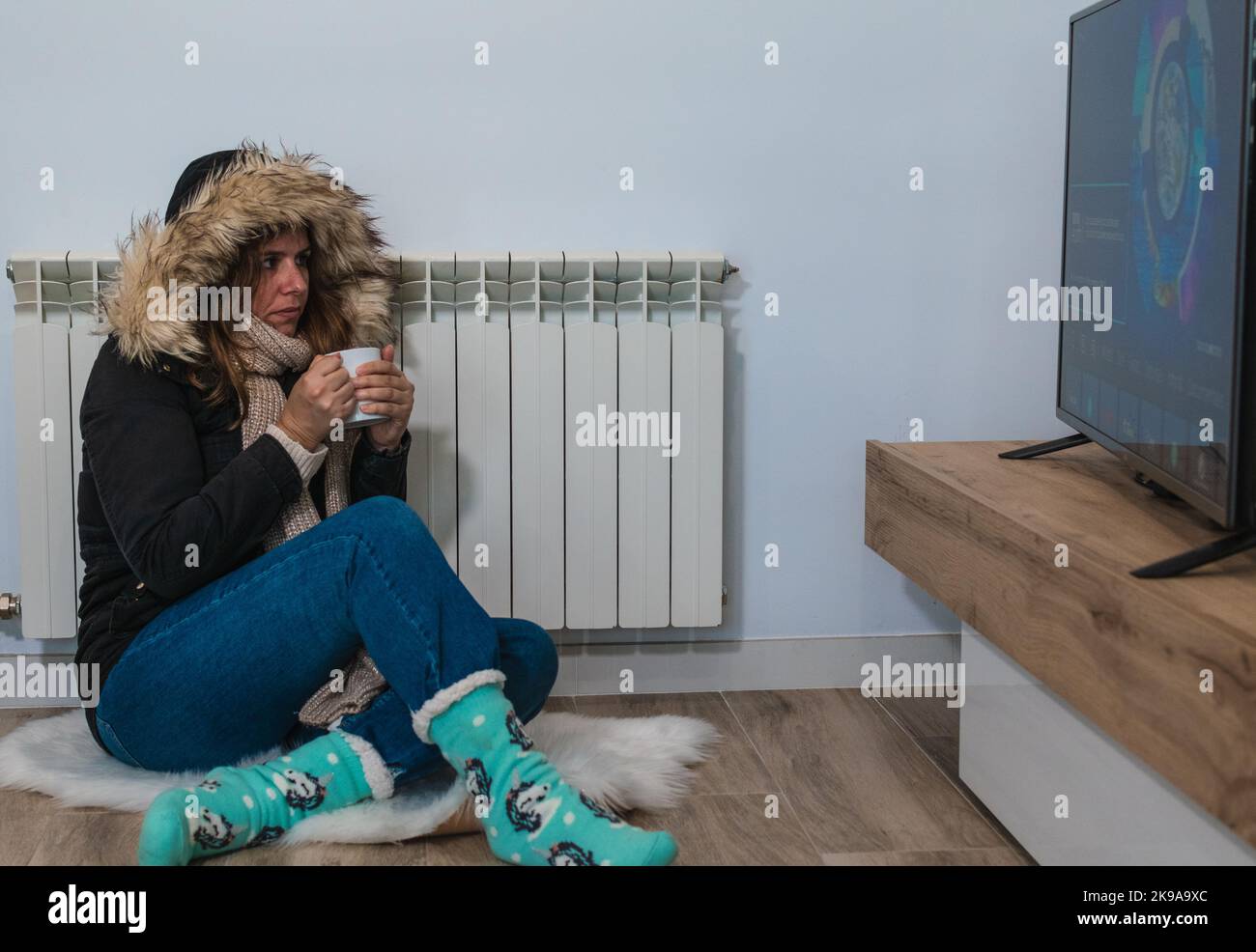 Frau, die sich zu Hause aufwärmt und ein heißes Getränk trinkt, während sie Fernsehen schaut Stockfoto