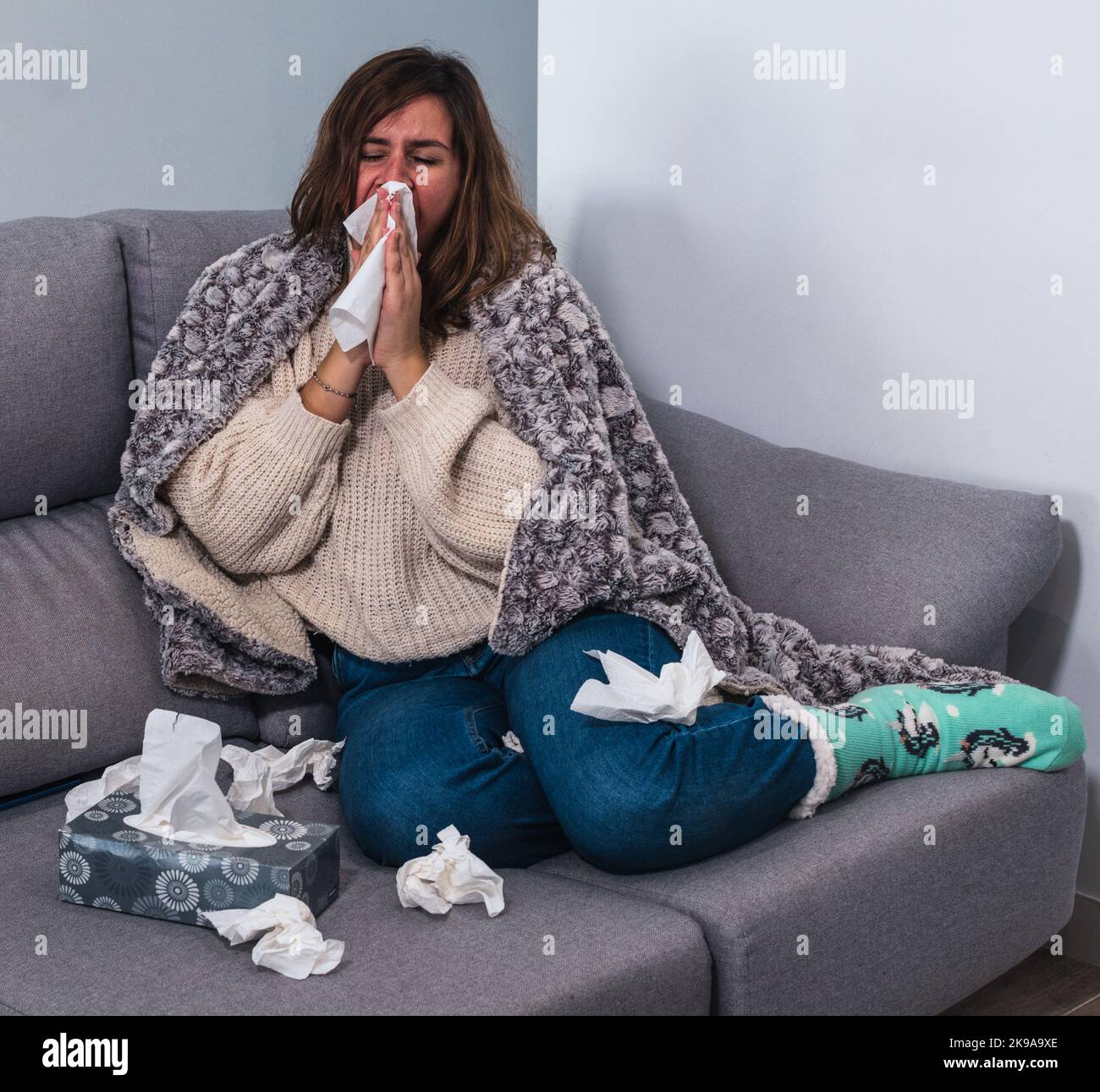Frau, die sich zu Hause wirklich krank fühlt, niest, umgeben von Geweben Stockfoto
