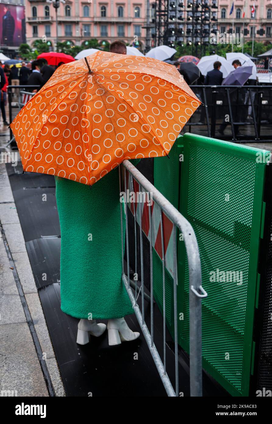 Frau mit grünem Kleid und orangefarbenem Regenschirm an einem regnerischen Tag - Mode im Street Style Stockfoto