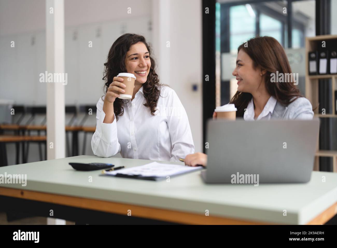 Zwei intelligente, multiethnische Geschäftsleute, die mit einem Laptop zusammenarbeiten, während sie im Büro über Jobnachrichten sprechen. Stockfoto