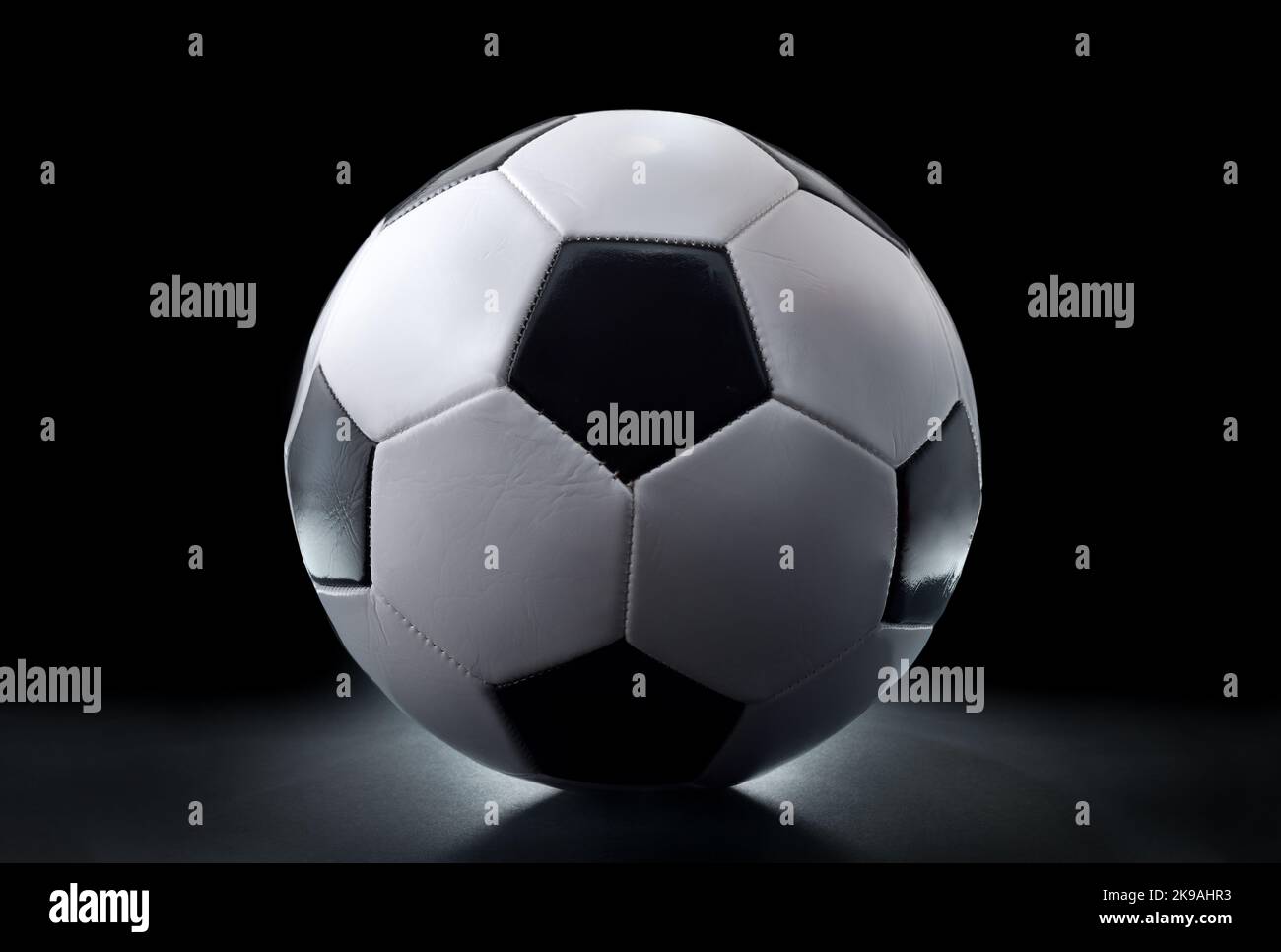 Detailansicht des klassischen schwarzen und weißen Lederfußballs isoliert auf dem Tisch und schwarzem Hintergrund. Vorderansicht. Stockfoto