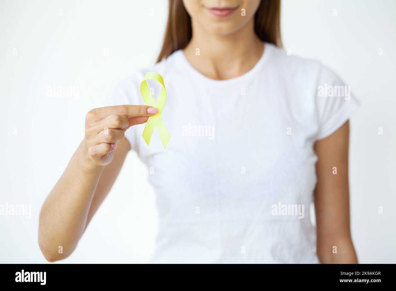 Nahaufnahme einer Frau im weißen T-Shirt, die ein gelbes Bewusstseinsband in ihren Händen hält und zeigt Stockfoto