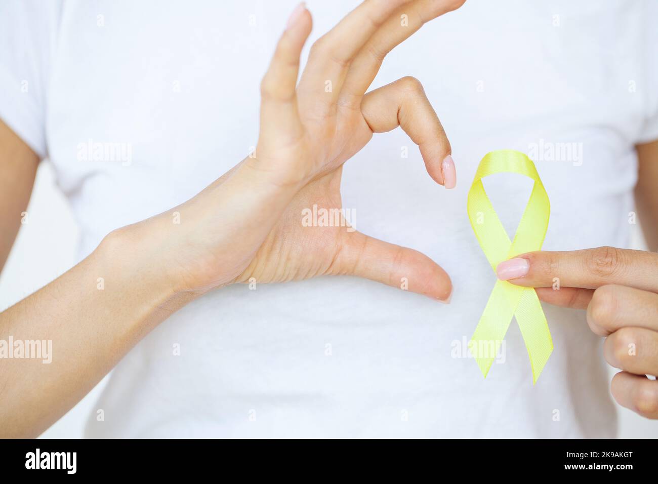 Nahaufnahme einer Frau im weißen T-Shirt, die ein gelbes Bewusstseinsband in ihren Händen hält und zeigt Stockfoto