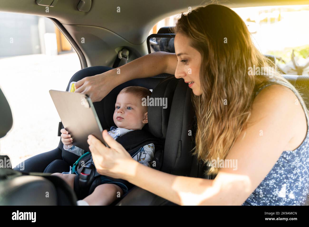 Mutter und Sohn, die mit dem Auto auf den Rücksitzen unterwegs sind und ein digitales Tablet verwenden Stockfoto