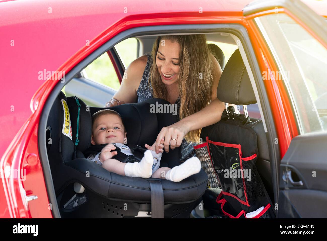 Mutter schnallt ihren Sohn auf den Autositz und legt seinen Sicherheitsgurt an Stockfoto