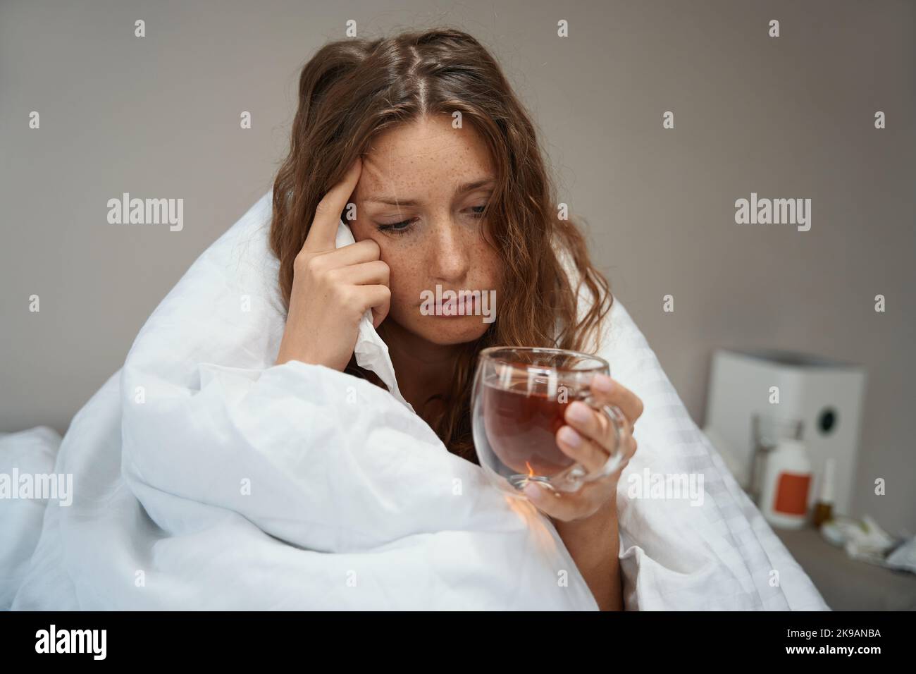 Frau, die im Bett saß und mit einer Decke mit einer Tasse Tee bedeckt war Stockfoto