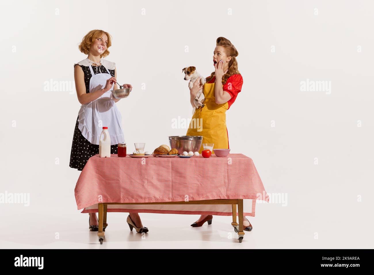 Porträt zweier eleganter, stilvoller Frauen, die gemeinsam kochen und auf weißem Hintergrund über Gerüchte diskutieren Stockfoto