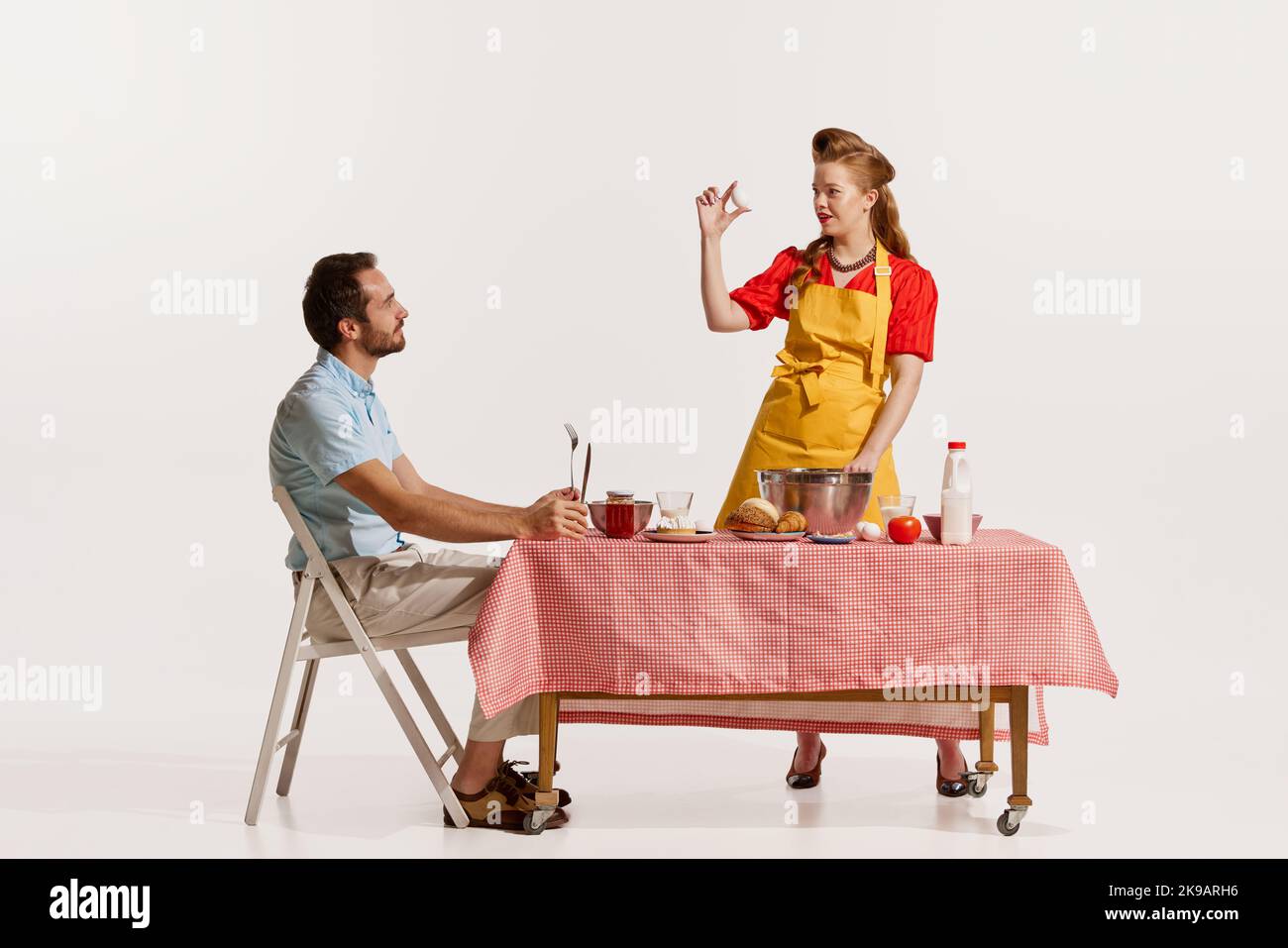 Porträt einer schönen Frau, die kocht, backt und Mann sitzt am Tisch isoliert auf weißem Hintergrund Stockfoto