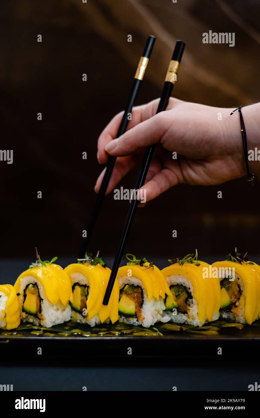 Hand hält Essstäbchen über Mango Maki mit Avocado Stockfoto