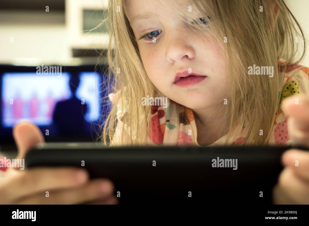 Kleines Mädchen auf Smartphone und Fernseher suchen. Handy-sucht im Kinderkonzept. Stockfoto