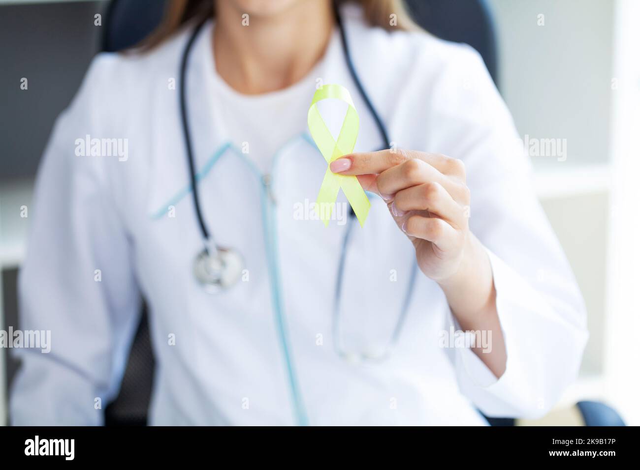 Nahaufnahme einer Frau im weißen T-Shirt, die ein gelbes Bewusstseinsband in ihren Händen hält und zeigt Stockfoto