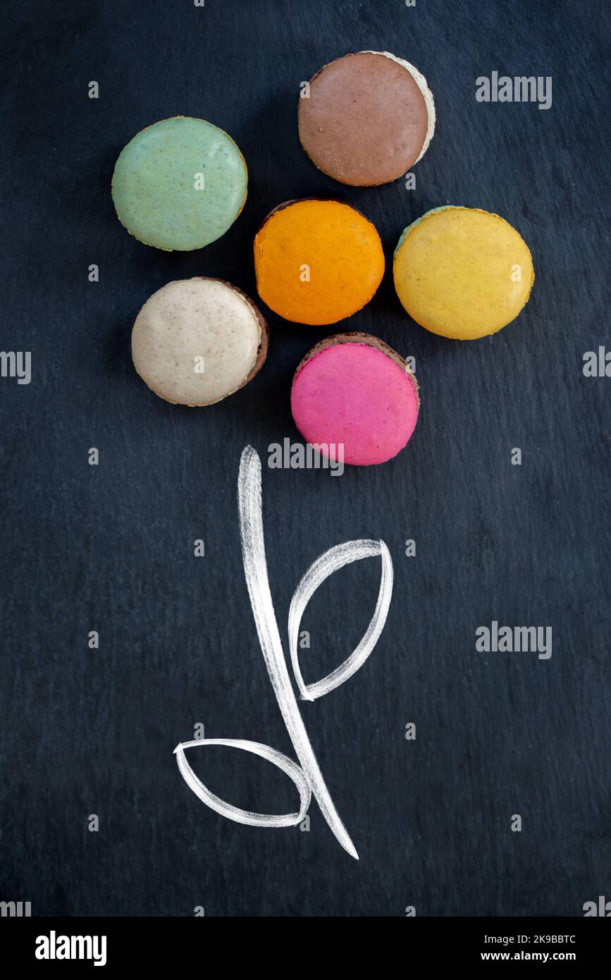 Anordnung französischer Macarons in Form einer Blume auf schwarzem Schieferhintergrund, kreatives Konzept zur Einrichtung von Speisen Stockfoto