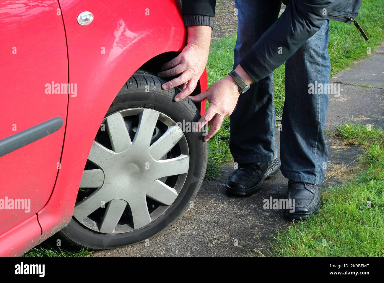 Reifenprofil an einem Kraftfahrzeug prüfen. Mann überprüft die Tiefe seiner Reifen mit den Händen, um sicherzustellen, dass sie legal sind. Stockfoto