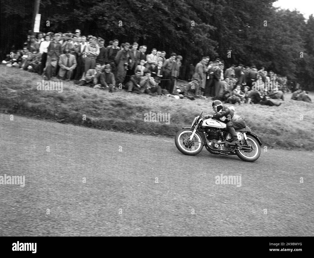 1954, historisch, ein männlicher Konkurrent auf einem Norton Motorrad auf der Rennstrecke Oliver's Mount Road in Scarborough, beobachtet von Zuschauern, die höher auf dem Kurs auf dem Rasen stehen, England, Großbritannien. Die hügelige Rennstrecke am Oliver's Mount ist Englands einzige natürliche „Road“-Rennstrecke und in dieser Zeit waren die Veranstaltungen als die Scarborough Races bekannt. Stockfoto