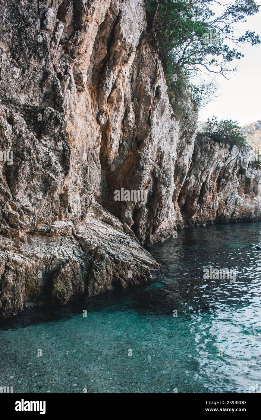 Korfu, Griechenland. Ein riesiger Felsen am Strand mit blauem Wasser, auf dem grüne Pflanzen und Bäume wachsen. Stockfoto