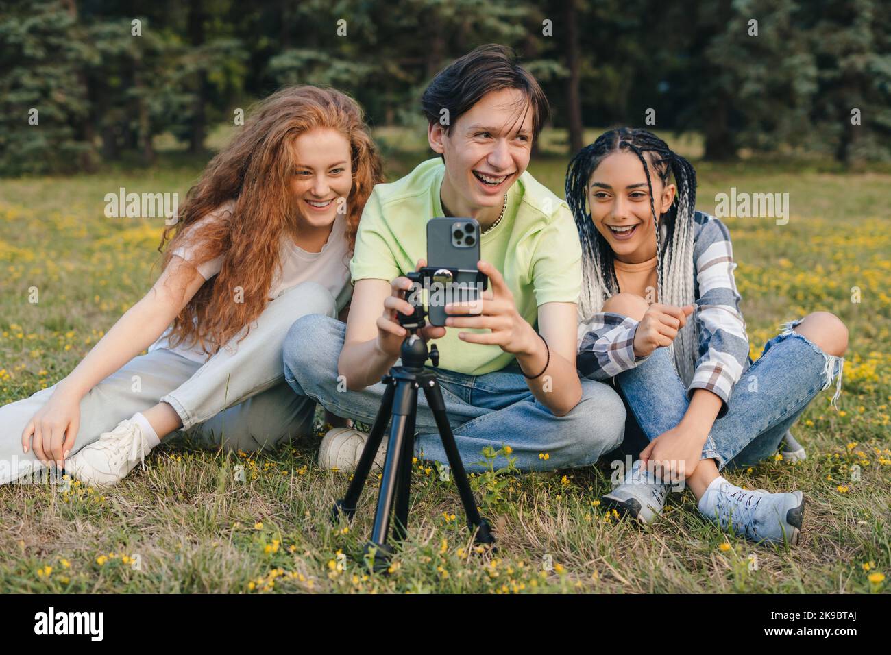 Drei Freunde Influencer, die Videos aufnehmen, während sie auf grünem Gras sitzen. Blogger streamen online vom Campus. Video-Live-Streaming Stockfoto