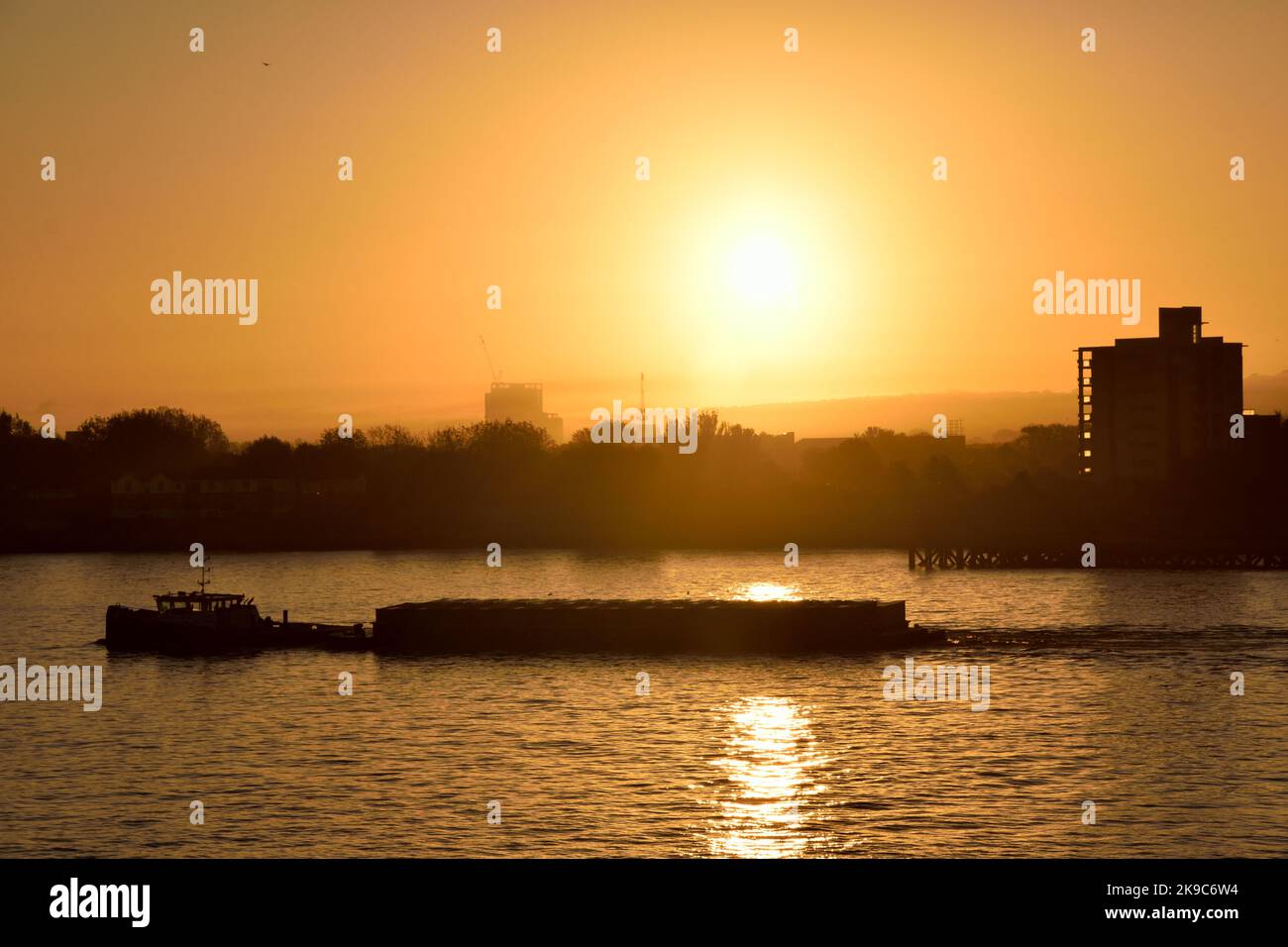 Herbstlicher Sonnenaufgang über der Themse im Osten Londons mit einem vorbeifahrenden Schlepper Stockfoto