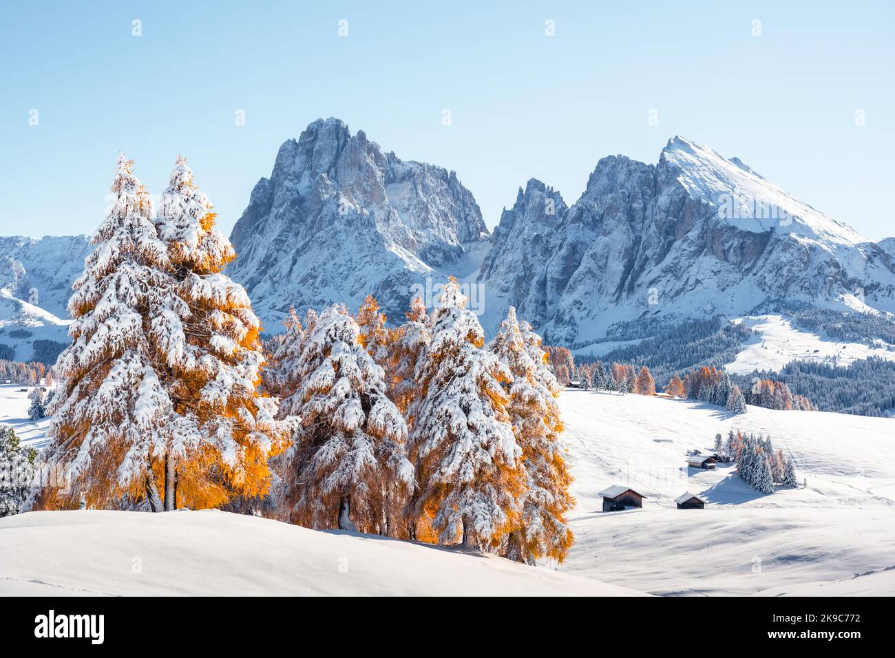 Malerische Landschaft mit kleiner Holzhütte auf der Seiser Alm bei Sonnenaufgang. Seiser Alm, Dolomiten, Italien. Verschneite Hügel mit orangefarbener Lärche und Langkofelgruppe Stockfoto