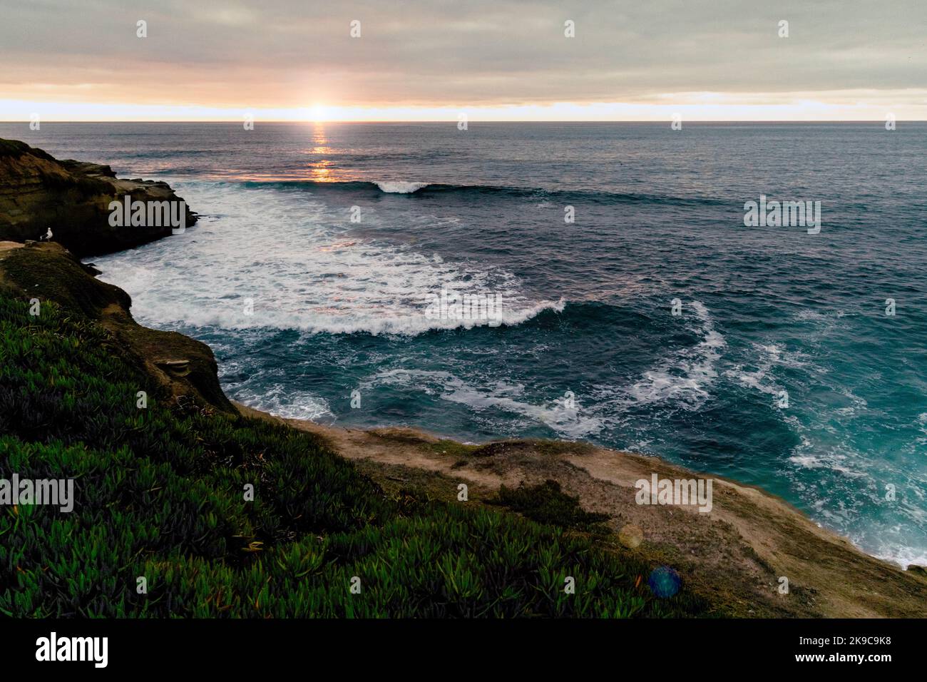 Atemberaubendes Sonnenuntergangsfoto, das in La Jolla, Kalifornien, aufgenommen wurde und Klippen, Wellen und eine Bucht zeigt. Landschaftsfotografie bei Sonnenuntergang mit Grün, Blau und Orangen. Stockfoto