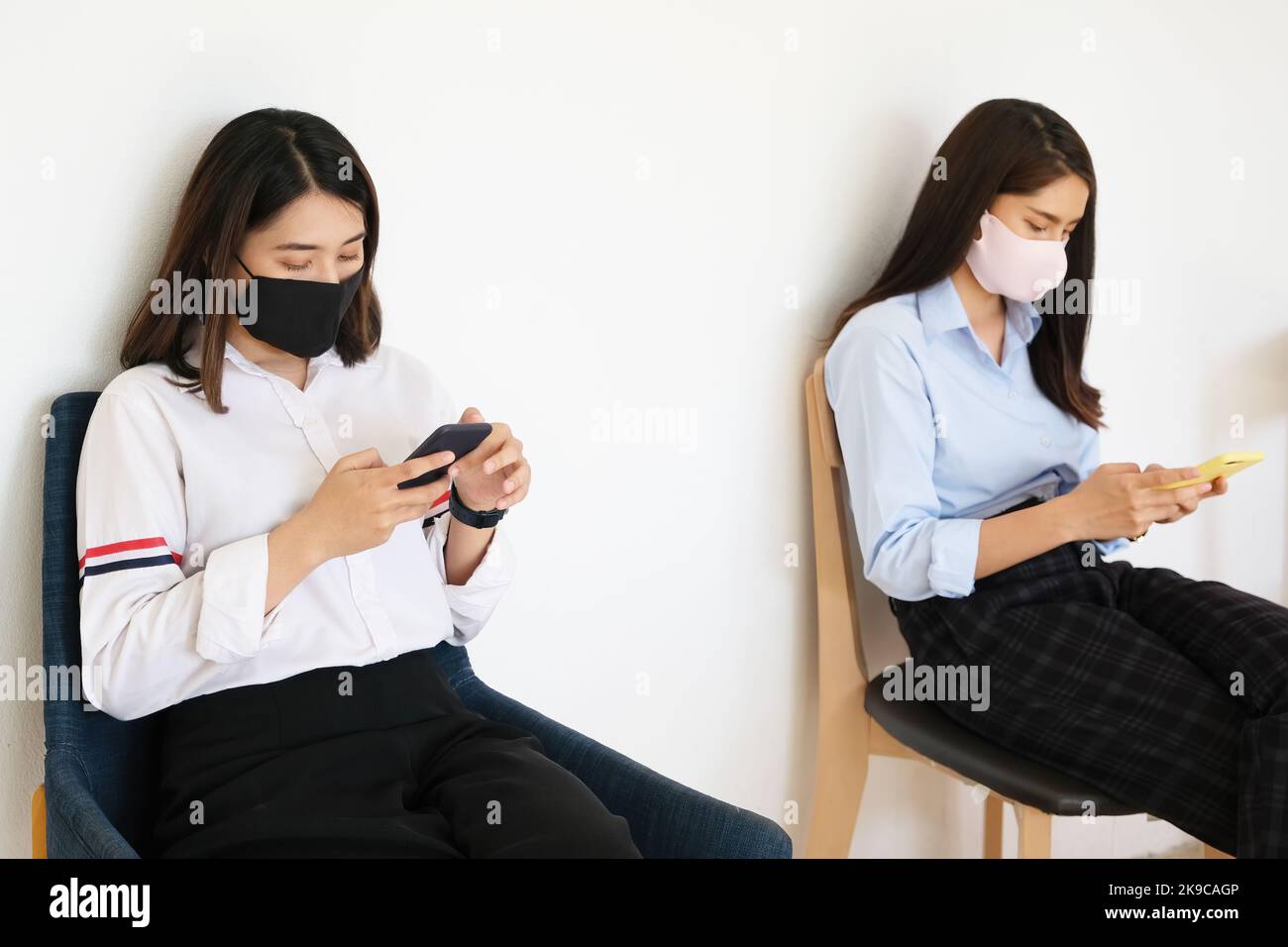 Konzept der sozialen Distanzierung, zwei Frauen tragen Masken und Distanzierungen, während sie auf Mobiltelefonen sitzen, und folgen dem sozialen Trend des Coronavirus. Stockfoto