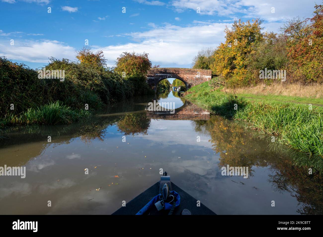 Der Bug eines traditionellen Kutschers am Kennet und Avon-Kanal mit Herbstfarben und einer fernen Steinbrücke. Stockfoto